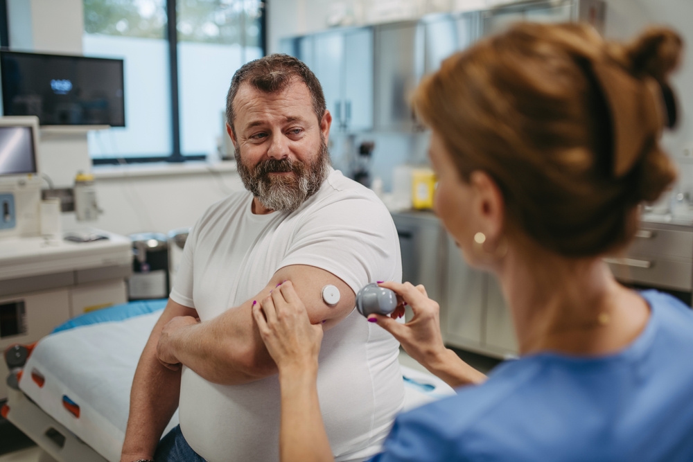 Doctor,Applying,A,Continuous,Glucose,Monitor,Sensor,On,Patient’s,Arm. A doctor applying an insulin pump to a patient