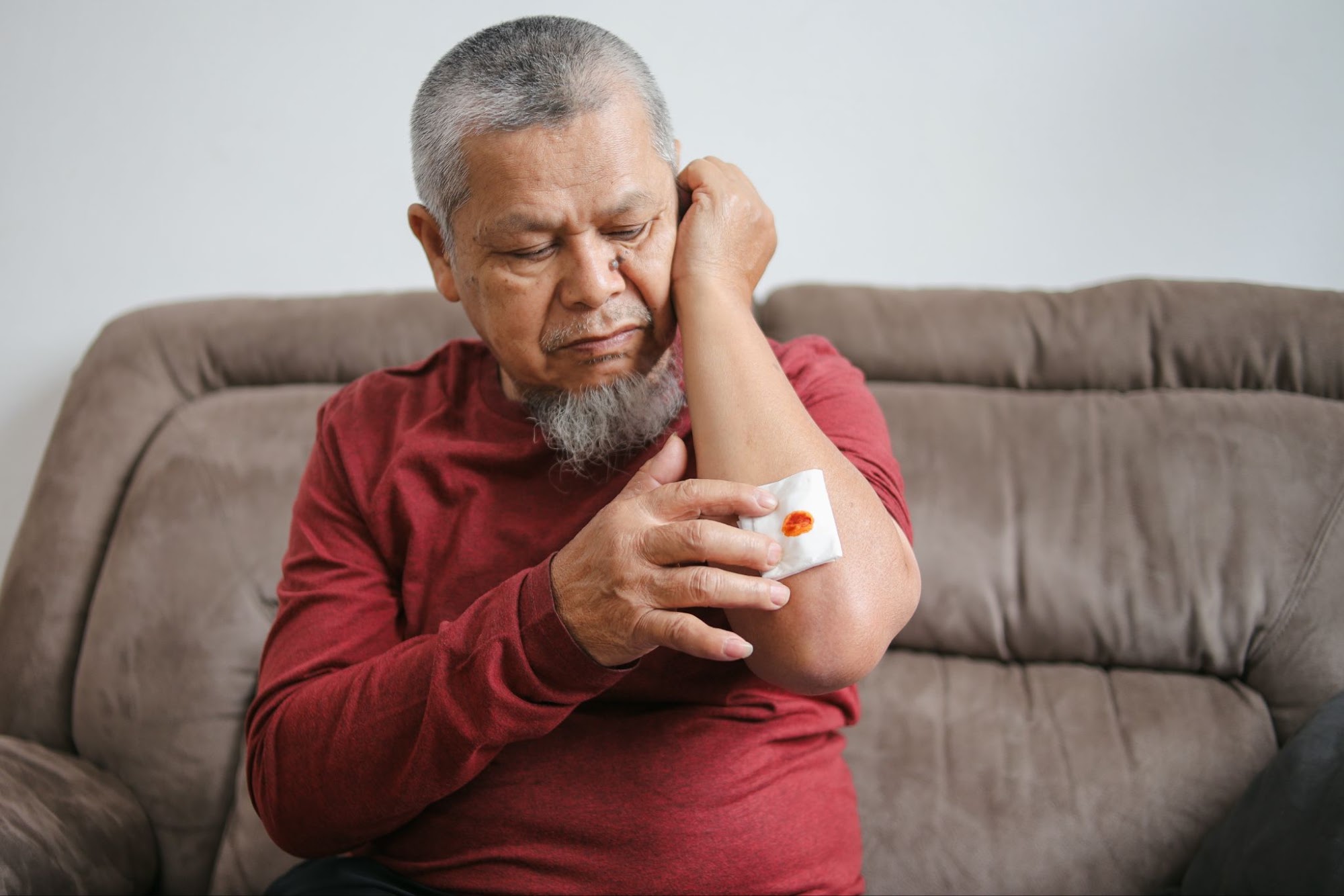Older man applying a sticking plaster to a wound on his arm